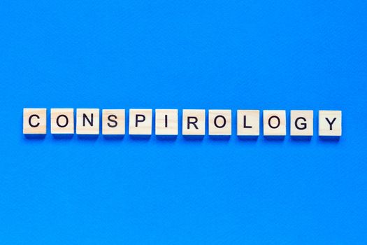 Conspirology - words made of wooden blocks with letters, secret plan of powerful people, conspiracy theory concept, top view blue background.