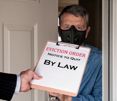 Open front door with man in suit handing an eviction notice to a defaulting renter with face mask during coronavirus epidemic