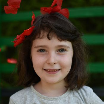 Portrait of little girl among red petals on a dark green background, square image