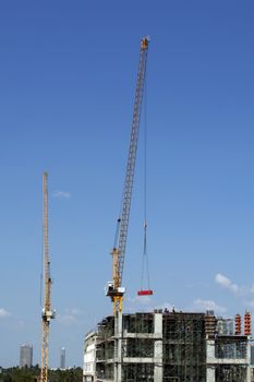Crane lifting material for building construction on bright blue sky.