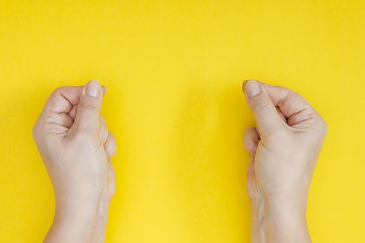 Hands with clenched fingers in a pinch on a yellow background