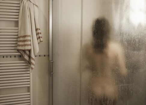 Sexy naked brunette woman take a shower inside the shower cabin seen through foggy glass in her modern design bathroom