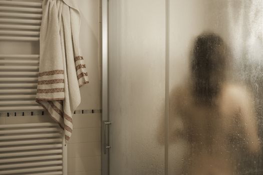 Sexy naked brunette woman take a shower inside the shower cabin seen through foggy glass in her modern design bathroom