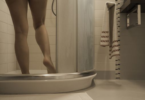Sexy naked woman's legs entering the foggy glass shower cabin in her modern design bathroom