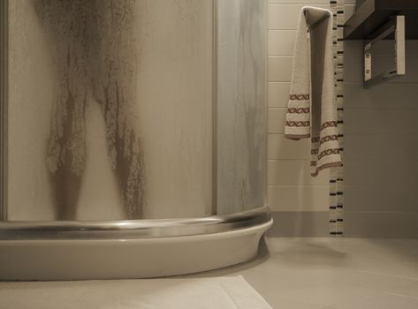 Sexy naked woman's legs inside the shower cabin behind the fogged glass door in her modern design bathroom