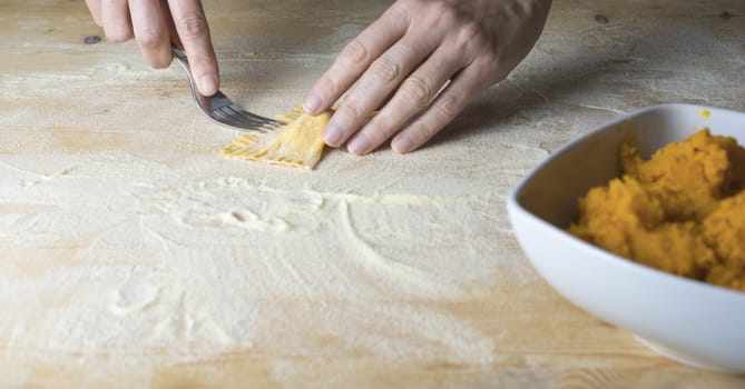 Closeup process making ravioli vegan homemade pasta. Housewife cook closes with a fork 'tortelli di zucca', traditional italian pasta, woman cooking food on kitchen