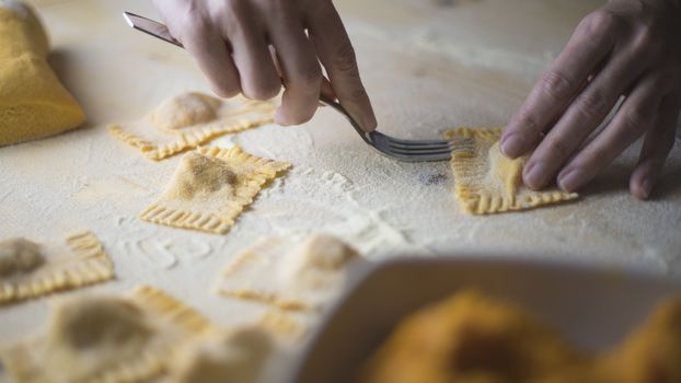 Closeup process making ravioli vegan homemade pasta. Housewife cook closes with a fork 'tortelli di zucca', traditional italian pasta, woman cooking food on kitchen