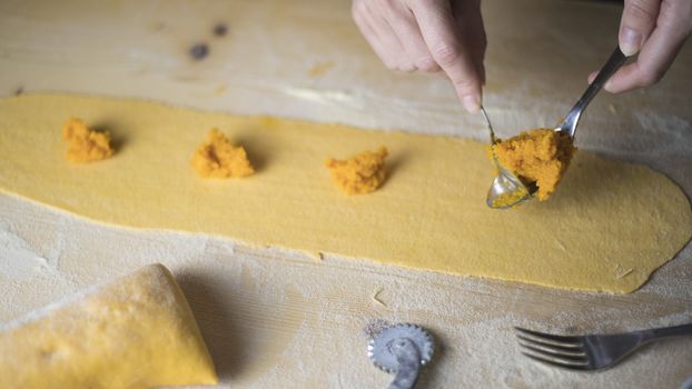 Closeup process making ravioli vegan homemade pasta. Housewife cook place the filling of the 'tortelli di zucca' on the pastry, measuring it with a spoon, on light wooden table