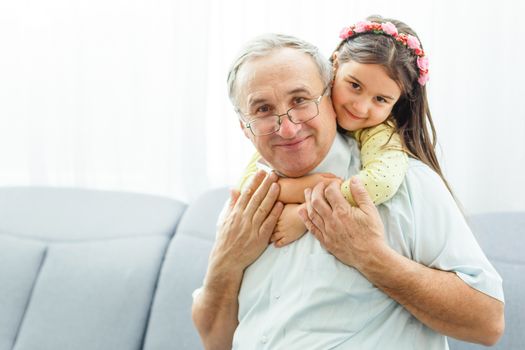 The happy girl hugs a grandfather on the sofa