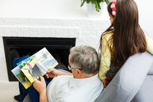 Granddaughter and grandfather watching photos together in a photo album at home