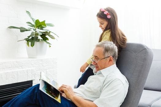 Granddaughter and grandfather watching photos together in a photo album at home