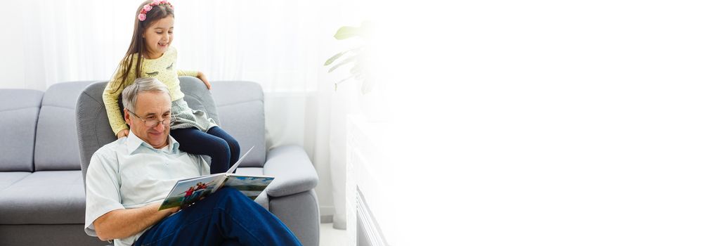 Grandfather and granddaughter on sofa at home. Grandpa and children are watching photos in album.