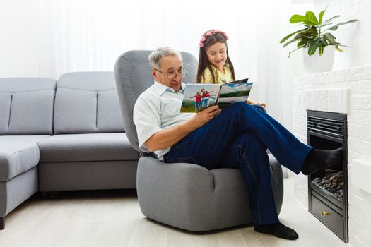 Granddaughter and grandfather watching photos together in a photo album at home