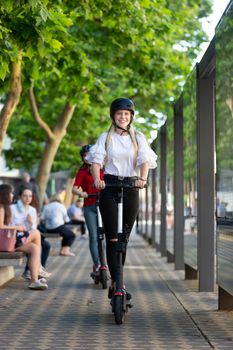 Trendy fashinable teenager girls riding public rental electric scooters in urban city environment. New eco-friendly modern public city transport in Ljubljana, Slovenia.