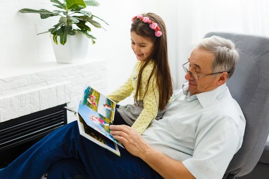 Granddaughter and grandfather watching photos together in a photo album at home