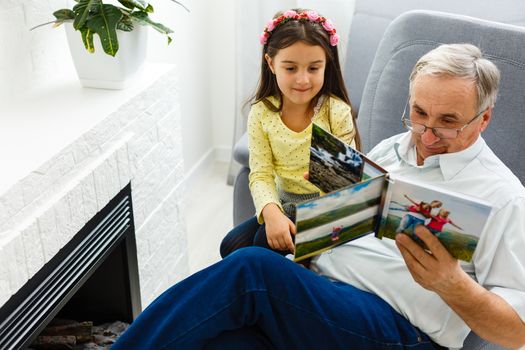 Granddaughter and grandfather watching photos together in a photo album at home