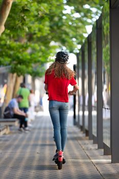 Rear view of girl riding public rental electric scooter in urban city environment. New eco-friendly modern public city transport in Ljubljana.