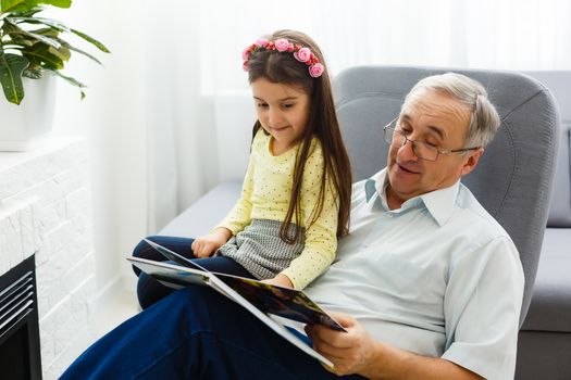 Granddaughter and grandfather watching photos together in a photo album at home