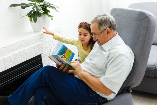 Granddaughter and grandfather watching photos together in a photo album at home