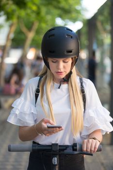 Trendy fashinable teenager, beautiful blonde girl using smartphone and renting modern electric scooter with an application. Urban transport concept.