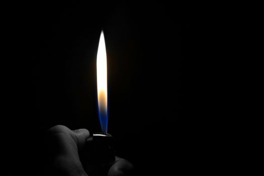 A hand lighting up a lighter with flame and dark background