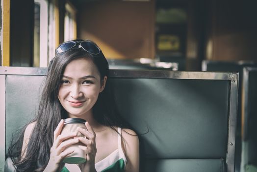 Asian woman traveler has drinking coffee in the train with happiness at Hua Lamphong station at Bangkok, Thailand.