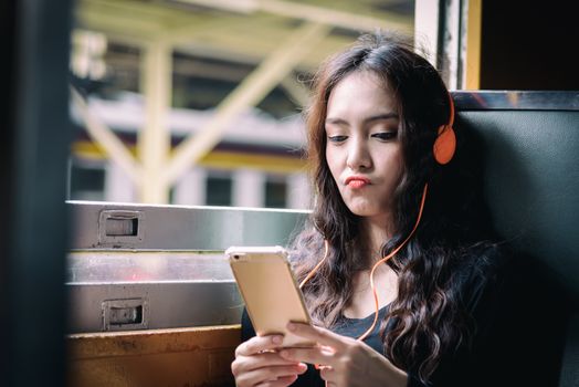 Asian woman traveler has listening music with phone and orange headphone inside the train at Hua Lamphong station at Bangkok, Thailand.