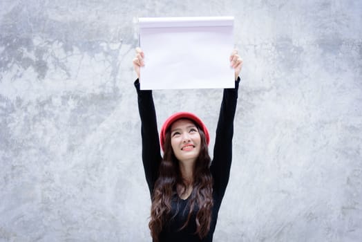 Asian woman with red hat and black clothes has holding a white paper on the grey stone wallpaper background with copy space.