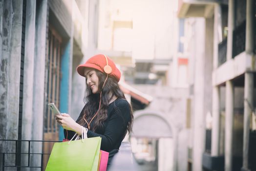 Asian portrait girl has happy and listening music with shopping colorful bags.