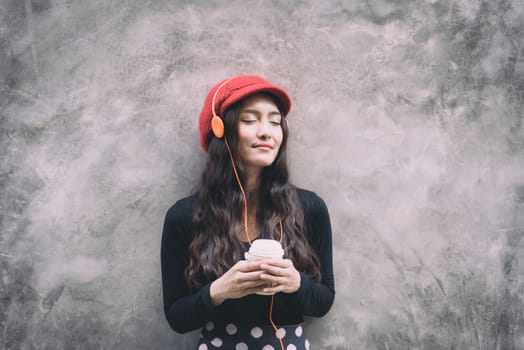 Asian portrait woman with red hat and black clothes has holding a cup of coffee with happiness and the grey stone wallpaper background.