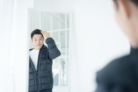 Asian handsome man looking at himself in mirror indoors