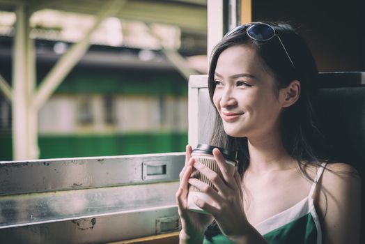 Asian woman traveler has drinking coffee in the train with happiness at Hua Lamphong station at Bangkok, Thailand.