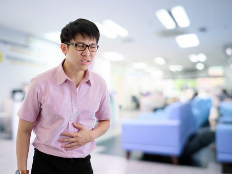 Asian businessman has standing with stomachache in hospital with light and interior background.