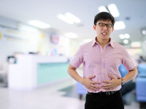 Asian businessman has standing with stomachache in hospital with light and interior background.