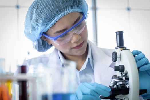 Asian yound student scientist researching with a microscope in a laboratory.