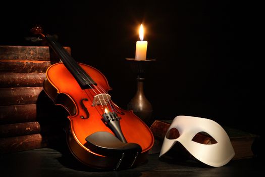 Nice violin near Venetian mask and candle against black background