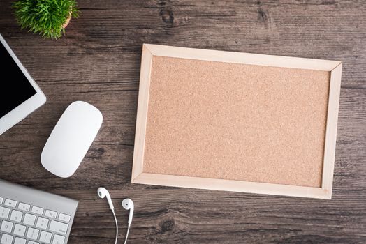 The office desk flat lay view with keyboard, mouse, tree, office pin board and earphone on wood texture background.