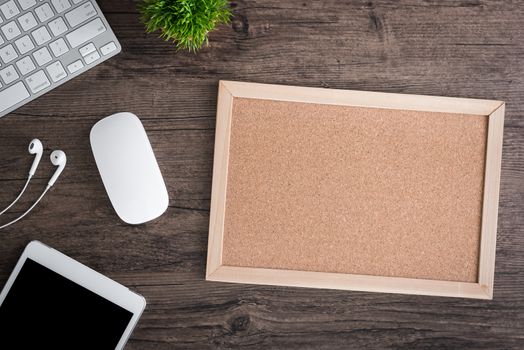 The office desk flat lay view with keyboard, mouse, tree, office pin board and earphone on wood texture background.