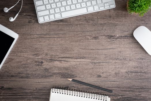 The office desk flat lay view with keyboard, mouse, tree, book, pencil and earphone on wood texture background.