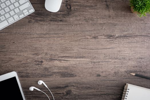 The office desk flat lay view with keyboard, mouse, tree, book, pencil and earphone on wood texture background.