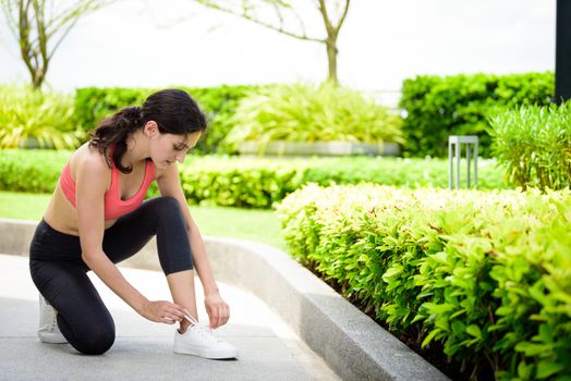 Beautiful woman runner has to tie white shoelaces in the garden.