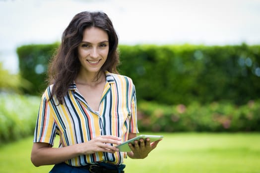 Portrait of a beautiful woman has playing tablet with smiling in the garden.