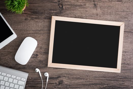 The office desk flat lay view with keyboard, mouse, tree, office pin board and earphone on wood texture background.