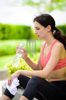 Beautiful woman runner has tired and rest for drinking water and a white towel to wipe her face after running in the garden.