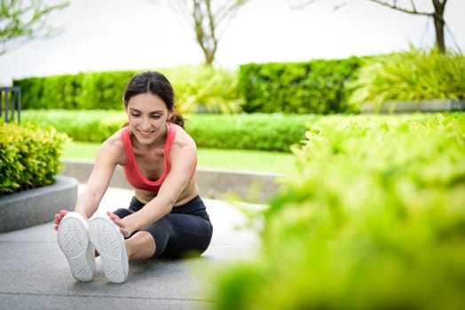 Beautiful woman runner has to warm up with stretching in the garden.