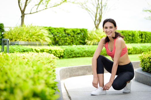 Beautiful woman runner has to tie white shoelaces in the garden.