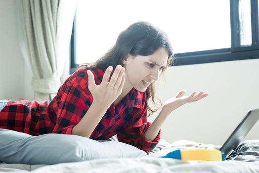 A beautiful woman has lain down on the bed at a condominium and shopping online on a laptop by the credit card with unhappy and worried in the morning.