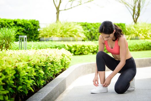 Beautiful woman runner has to tie white shoelaces in the garden.