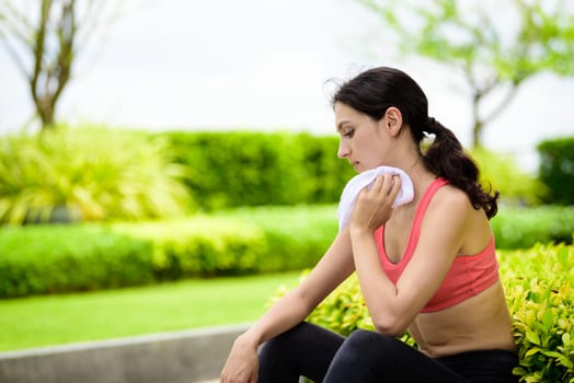 Beautiful woman runner has used a white towel wipe her face after running in the garden.