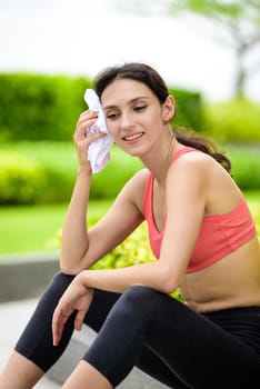 Beautiful woman runner has used a white towel wipe her face after running in the garden.